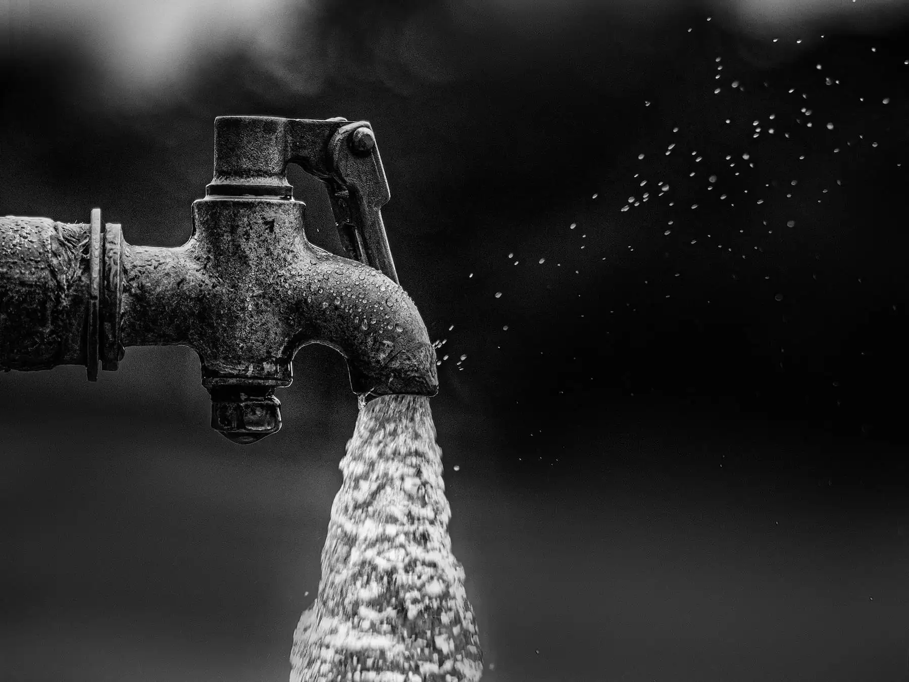 Wasserhahn mit fließendem Wasser in Schwarz-Weiß, Sinnbild für die tägliche Bereitstellung von Frischwasser.
