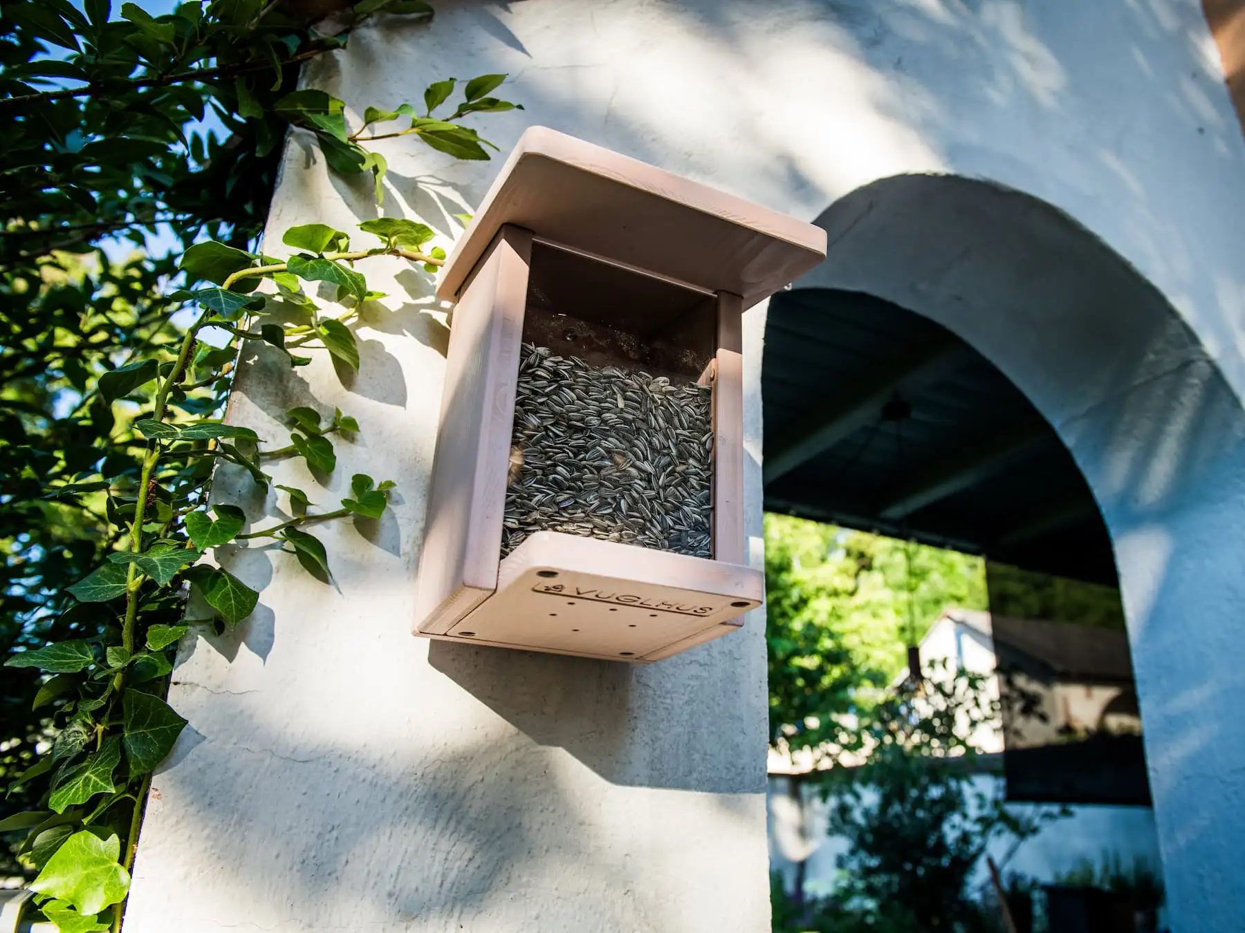 Hanehus Futterhaus mit Vogelfutter hängt an der Wand – ganzjährige Futterstelle für Gartenvögel.